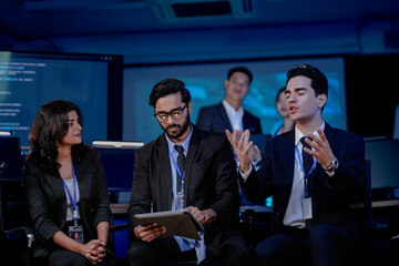 A diverse software engineering team in a SOC. An Indian developer holding a tablet discusses AI algorithm optimization and cybersecurity protocols. His team, including women and men,