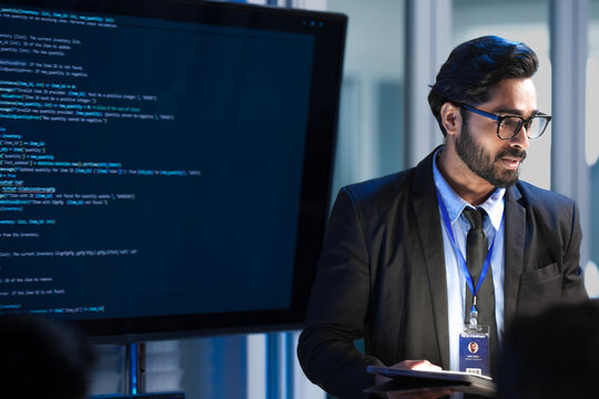 An Indian male software engineer or team lead discusses Python code for an AI algorithm. A developer in the audience raises their hand to ask a technical question during a code review.