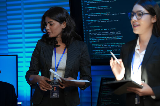 An Indian female developer leads a code review, holding a report. She explains a Python script for an AI or cybersecurity system to her team in a dark SOC Security Operations Center.