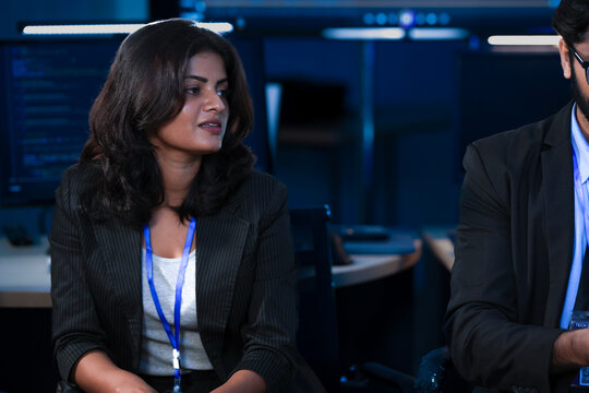 Two female software engineers, one Caucasian and one Indian, attend a technical briefing in a SOC. They analyze AI-driven cybersecurity data on a screen.