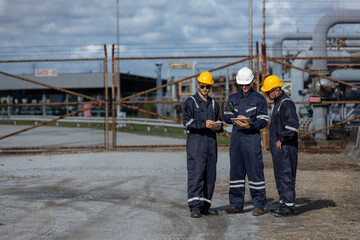 Group of industrial engineers wearing safety gear discussing work plans near secured facility gate, highlighting teamwork, planning, and field coordination in energy or petrochemical industries.