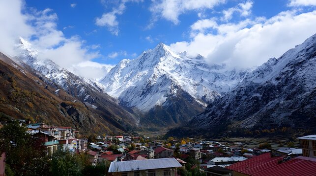 High snow-capped mountain peaks tower above a small valley settlement under a bright blue sky. - Powered by Adobe