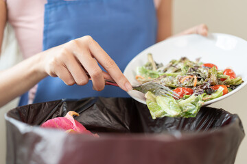 The housewife is throwing the leftover food from the meal into the bin