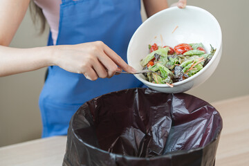 The housewife is throwing the leftover food from the meal into the bin
