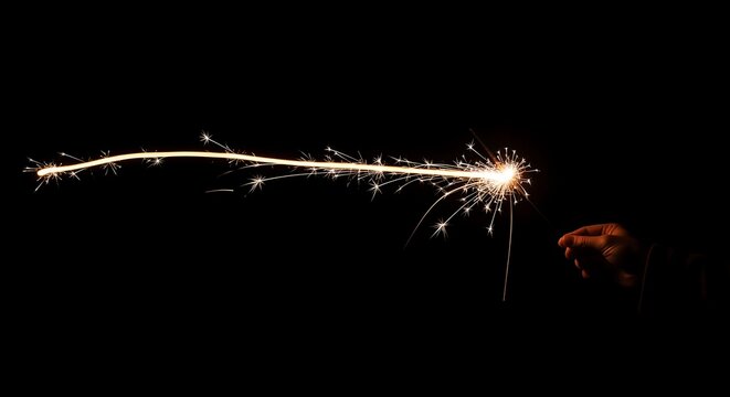Hand holding sparkler creating light trails in the dark night sky during celebration, creating magical and festive atmosphere.