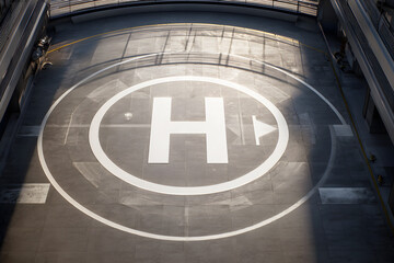 Helipad is marked with large clear 'H' symbol surrounded by safety markings and against urban or building backdrop. Aerial photograph showcasing modern helicopter landing pad from top-down perspective