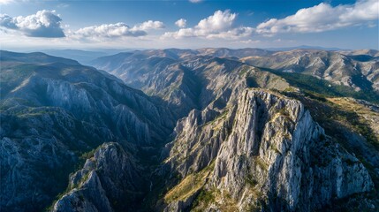 Fototapeta premium Elevated view captures vast mountainous landscape with deep canyon and scattered clouds