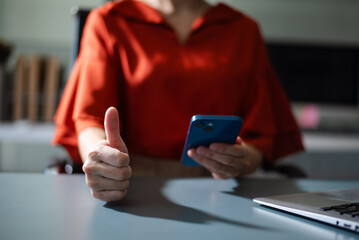 Person giving thumbs up while using smartphone. Symbol of success, approval, positive communication, and modern digital lifestyle.