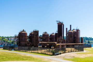 Side view of the a former oil plant fenced in and surrounded by a wide lawn under a clear blue sky. Taken while walking in the Seattle urban area on a clear July day, specifically in Gas Works Park.