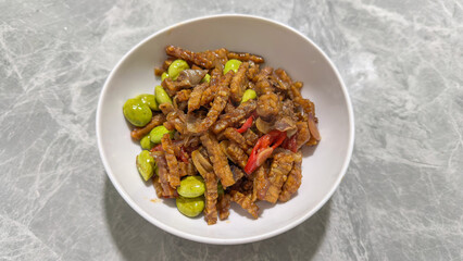 Stir Fried Tempeh with Petai Beans and Chili on White Bowl, Traditional Indonesian Food with Spicy Sweet Soy Sauce on Marble Table Background