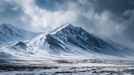 Towering snow-covered mountain range dominates a desolate winter landscape under dramatic sky