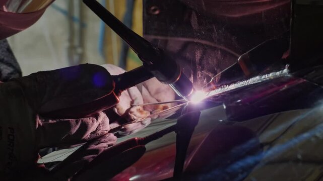 An industrious and technical mood is captured by a close-up of a welder in protective gear using a welding torch, with the bright arc and reflection visible in the shield and surrounding surfaces
