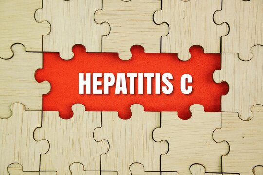 Wooden puzzle and red background with the word hepatitis c. an infectious disease caused by a hepatotrophic virus called Hepatitis C virus. Hepatitis C infection can cause swelling of the liver which 