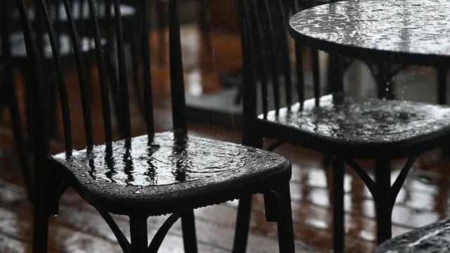 Heavy raindrops hit outdoor furniture, making water streams on surface. dark chairs and wet table. Close-up view of raindrops splashing on table and chair outside. rainy weather atmosphere.