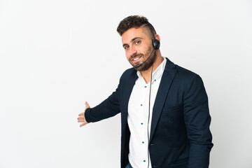 Telemarketer man working with a headset isolated on white background extending hands to the side for inviting to come