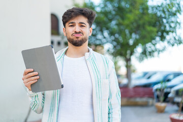 Handsome Arab man holding a tablet at outdoors with sad expression