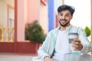 Handsome Arab man holding a take away coffee at outdoors with happy expression