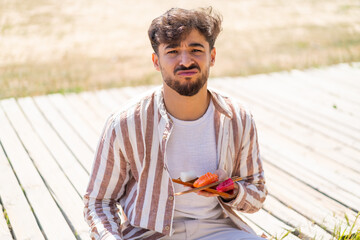 Handsome Arab man holding sashimi at outdoors with sad expression