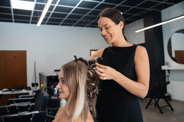 Fototapeta premium Hair stylist curling hair for a client at a modern salon during mid-afternoon