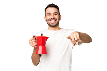 Young caucasian man holding coffee pot over isolated chroma key background points finger at you...