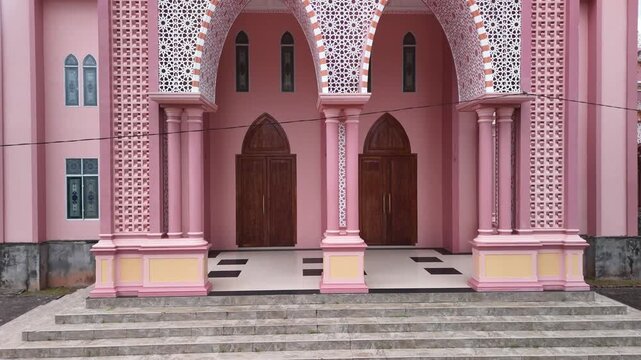 Aerial view of the pink AnNur Mosque in Bintan showcasing its elegant domes and reflection surrounded by lush greenery and tranquil water scenery