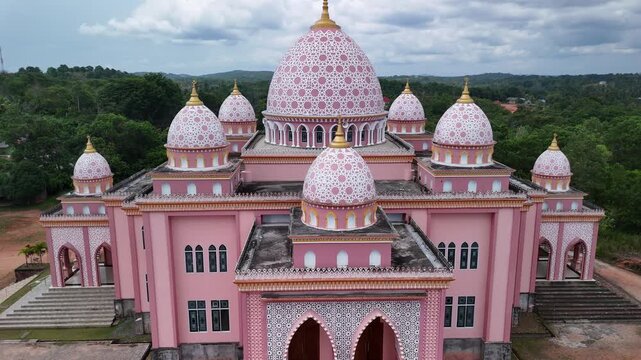 Aerial view of the pink AnNur Mosque in Bintan showcasing its elegant domes and reflection surrounded by lush greenery and tranquil water scenery