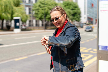Woman checking the time while waiting at a bus stop in a busy urban area during the day
