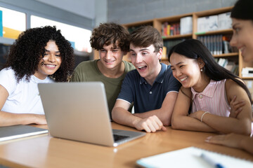High school students laughing and watching a laptop in library © Daniel