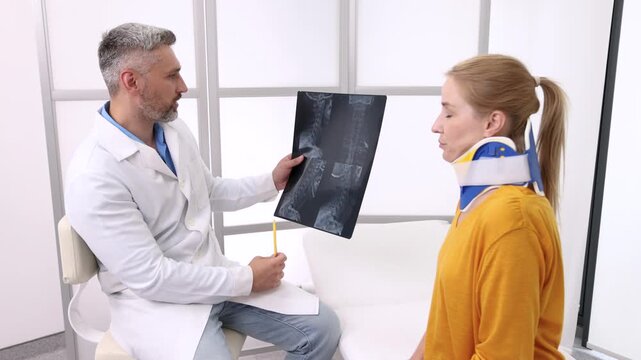 Adult woman with neck injury in a cervical brace during consultation with manual therapist who is looking at MRI of patient's neck