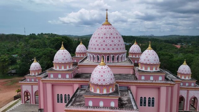 Aerial view of the pink AnNur Mosque in Bintan showcasing its elegant domes and reflection surrounded by lush greenery and tranquil water scenery