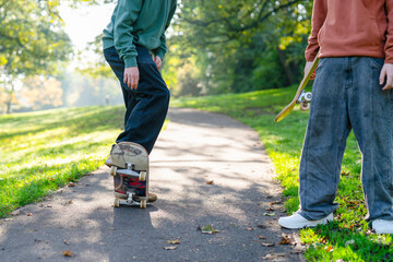Two young friends skateboarding on a sunny park path during autumn in the afternoon