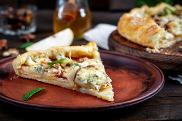 Baked galette or open pie with pear, blue cheese and nuts on the wooden table.