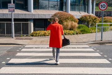 Person in bright red coat walking across a crosswalk on a sunny day in an urban area