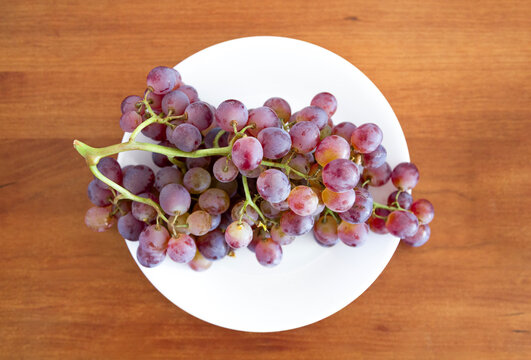 A bunch of purple grapes in a white plate on the table