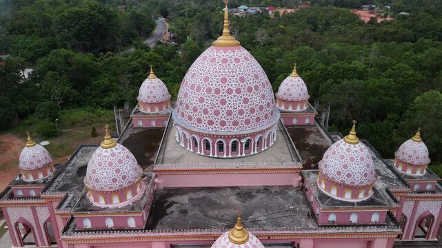 Aerial view of the pink AnNur Mosque in Bintan showcasing its elegant domes and reflection surrounded by lush greenery and tranquil water scenery