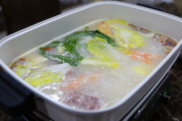 The hot pot is boiling and vegetables are cooking in the pot