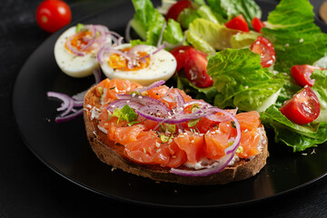 Delicious healthy breakfast - boiled egg, sandwich salmon and green salad. Balanced meal plate on dark background