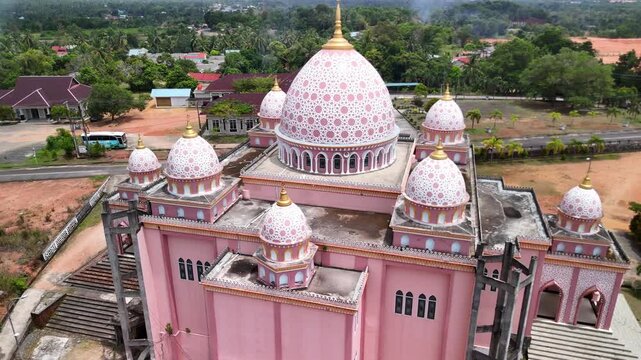 Aerial view of the pink AnNur Mosque in Bintan showcasing its elegant domes and reflection surrounded by lush greenery and tranquil water scenery