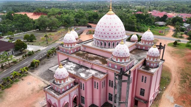 Aerial view of the pink AnNur Mosque in Bintan showcasing its elegant domes and reflection surrounded by lush greenery and tranquil water scenery