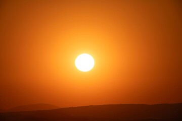 Bright sun setting over distant rolling hills with orange sky