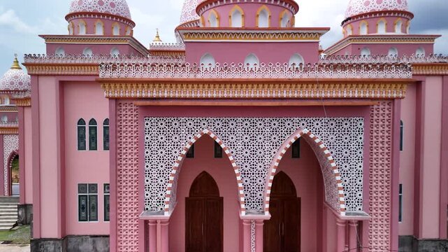 Aerial view of the pink AnNur Mosque in Bintan showcasing its elegant domes and reflection surrounded by lush greenery and tranquil water scenery
