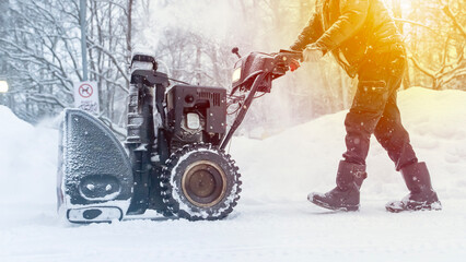 A man with a snow blower removes snow in the yard