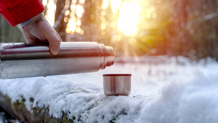 Tourist pouring hot tea or coffee from a thermos in a snowy sunny forest