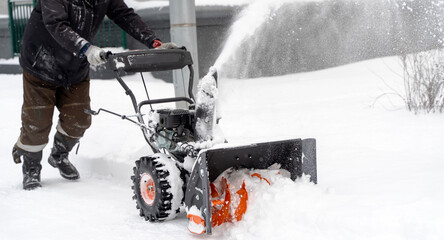 A man with a snow blower removes snow in the yard