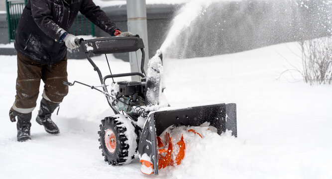 A man with a snow blower removes snow in the yard