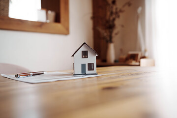 Miniature house model placed on real estate documents with a pen on a wooden table, symbolizing property investment and home ownership concept.
