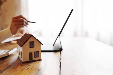 Person signing a real estate contract while holding a small house model, representing home ownership, property investment, and mortgage agreement.