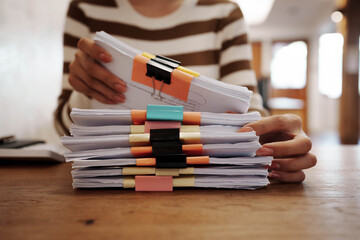 A person organizing stacks of documents with colorful binder clips on a wooden desk in a bright office environment.