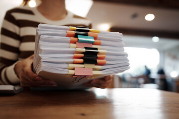 A person organizing stacks of documents with colorful binder clips on a wooden desk in a bright office environment.