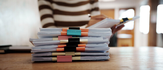 A person organizing stacks of documents with colorful binder clips on a wooden desk in a bright office environment.